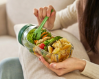 Person holding a glass container with a salad on a couch